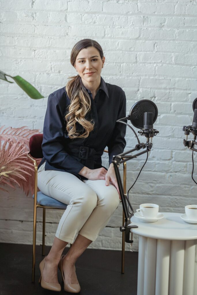 Woman in a stylish podcast setup with microphones and beverages.